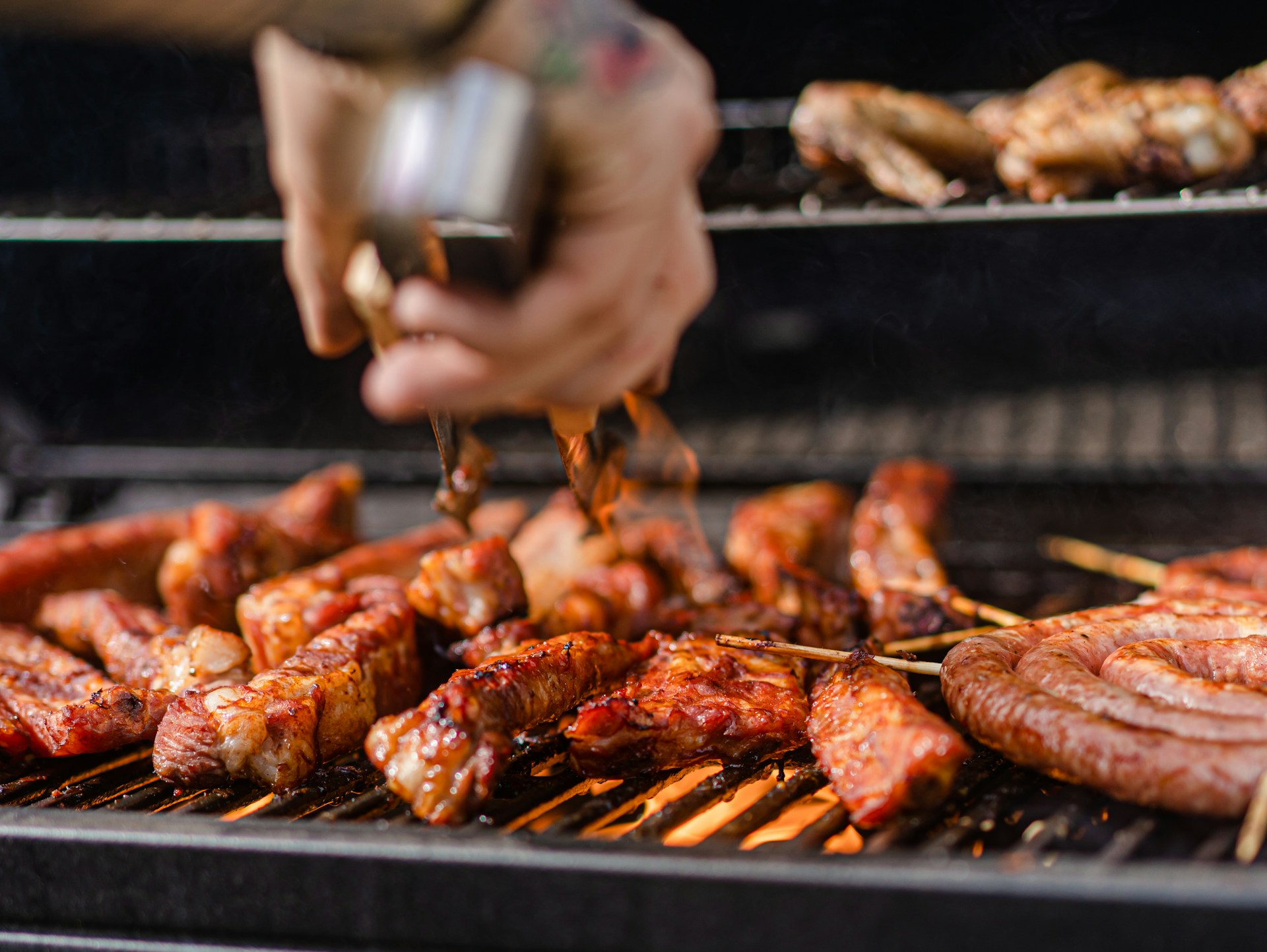 Costillas glaseadas, salchicha parrillera en espiral y alitas cocinándose a la llama