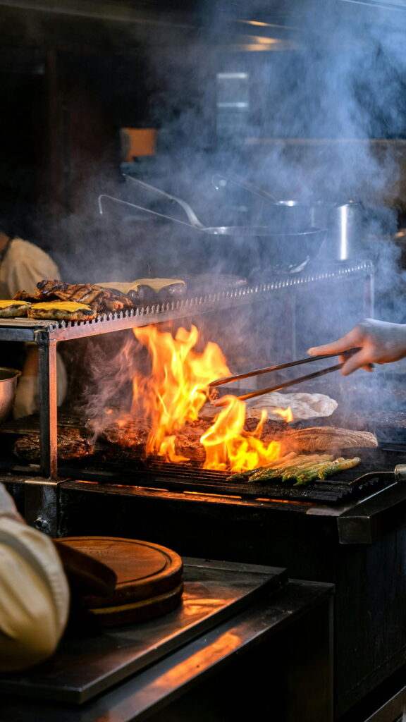 Chef asando carnes, hamburguesas y espárragos a la llama en parrilla profesional Live BBQ