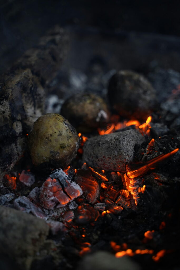 Patatas enteras asándose entre brasas y ascuas, guarnición tradicional a la brasa
