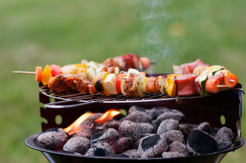 Brochetas de carne y verduras a la parrilla con llamas y humo en barbacoa de carbón